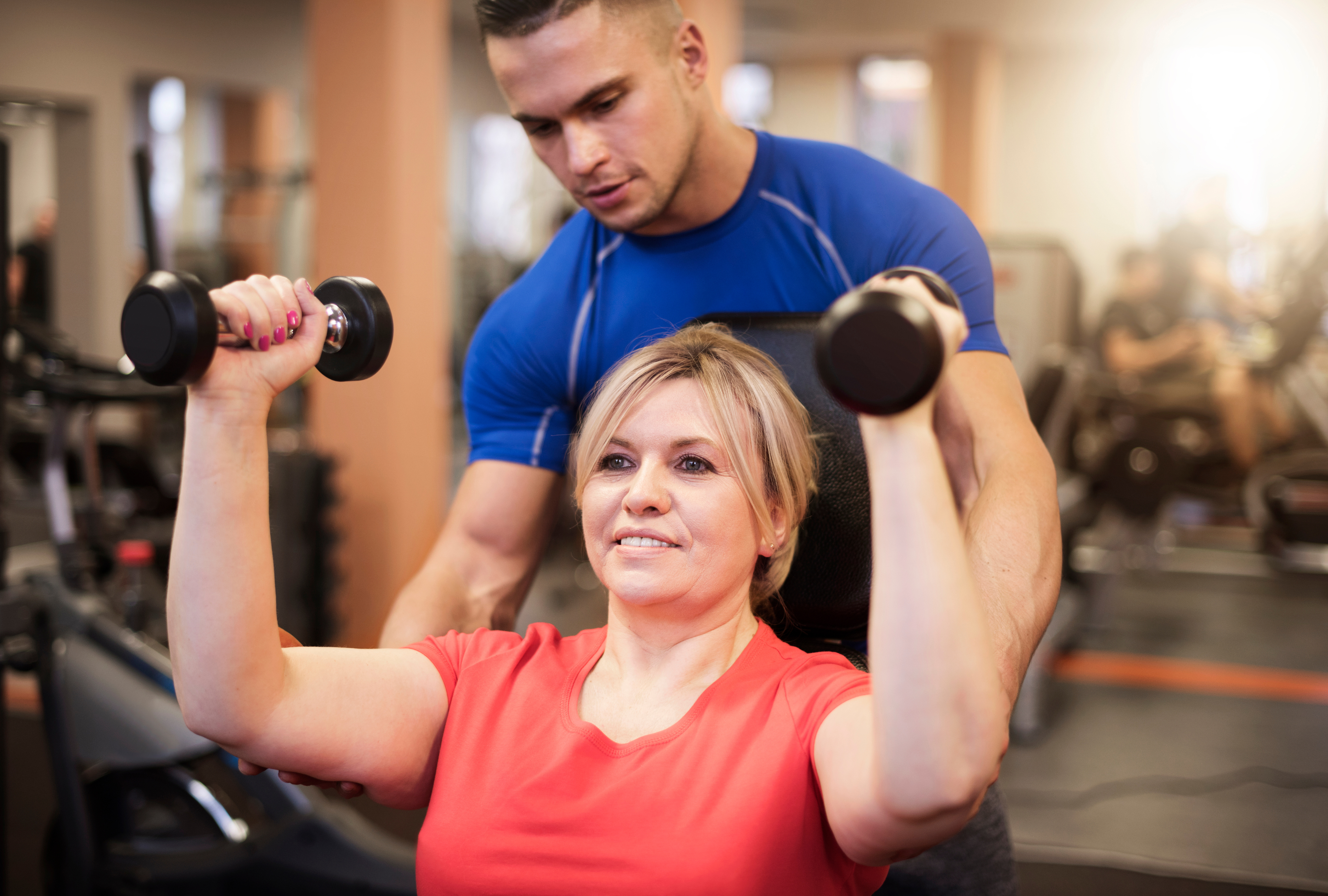A personal trainer helps a woman lift weights as part of Weigh to Change