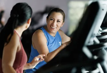 two women walking on treadmills and engaged in conversation