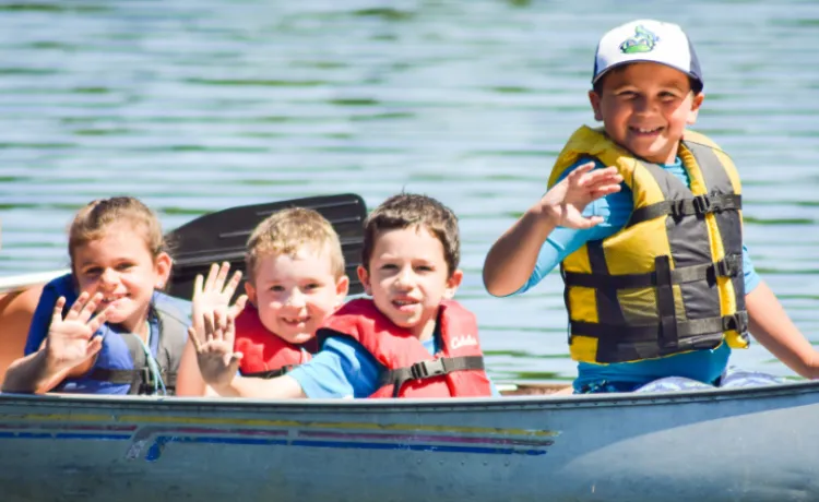 group of young kids waving from canoe on the lake