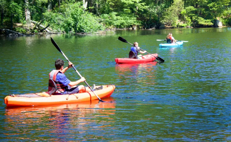 three individuals kayaking on a reservoir on a sunny day