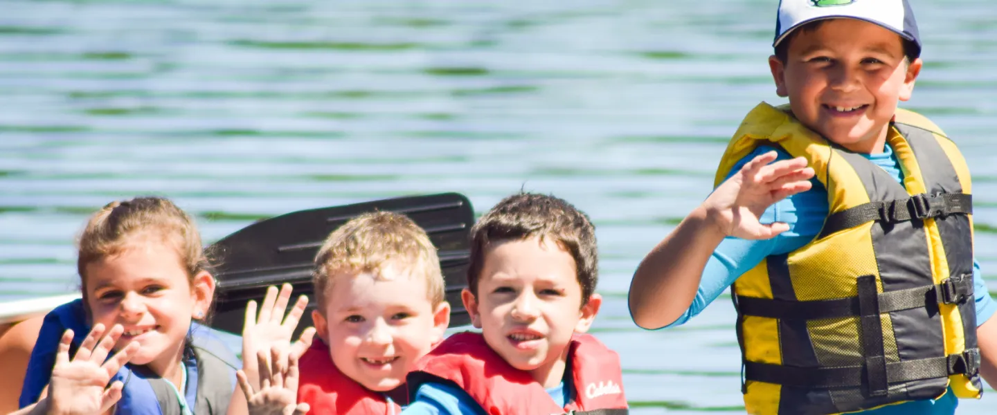image of young kids waving from a canoe