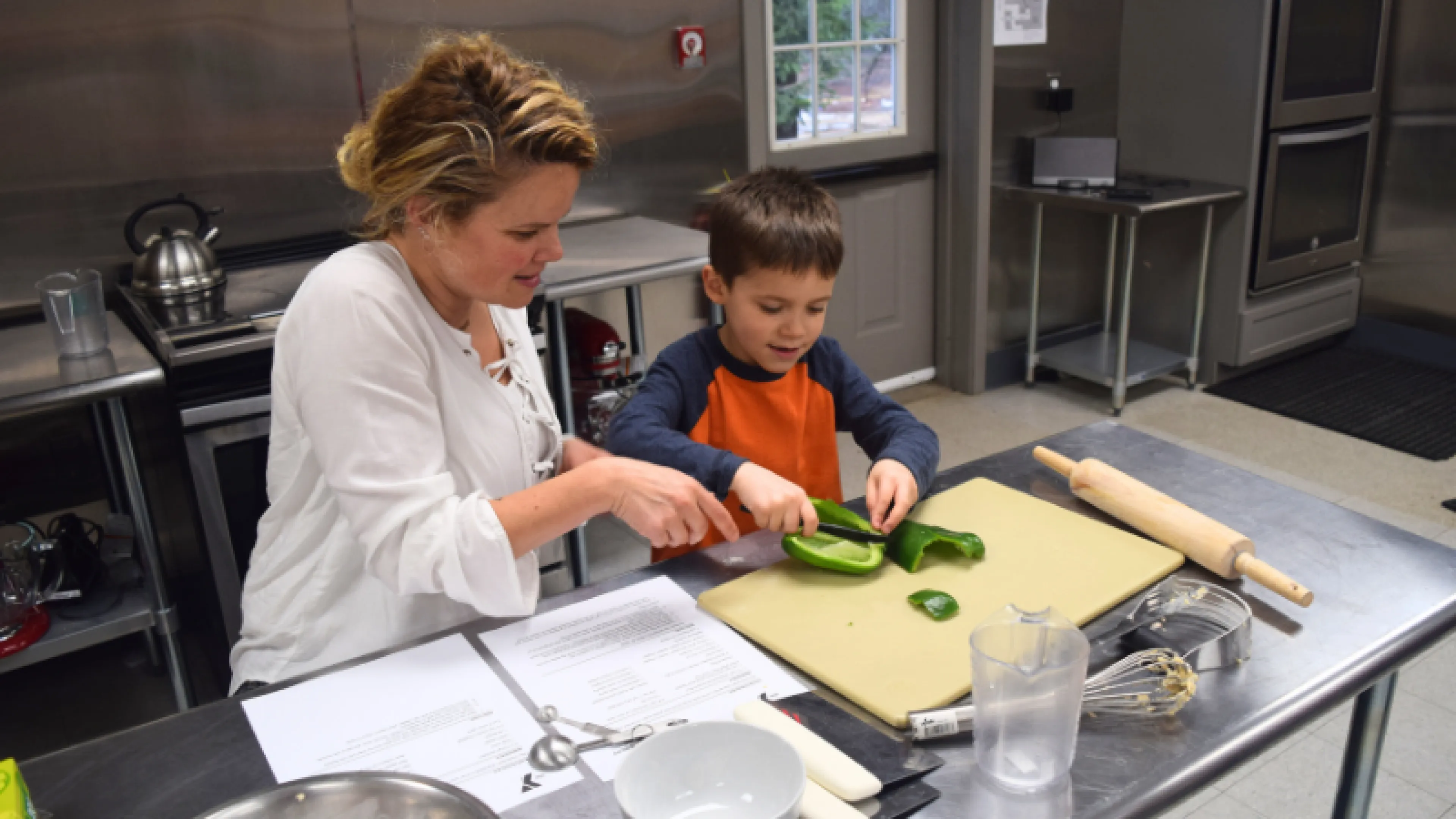 mother teaching young son how to cut a pepper during cooking class
