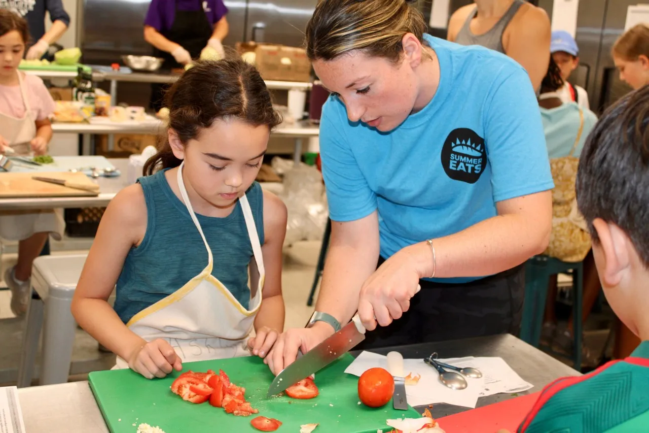 image of camper learning how to cut tomatoes by teacher
