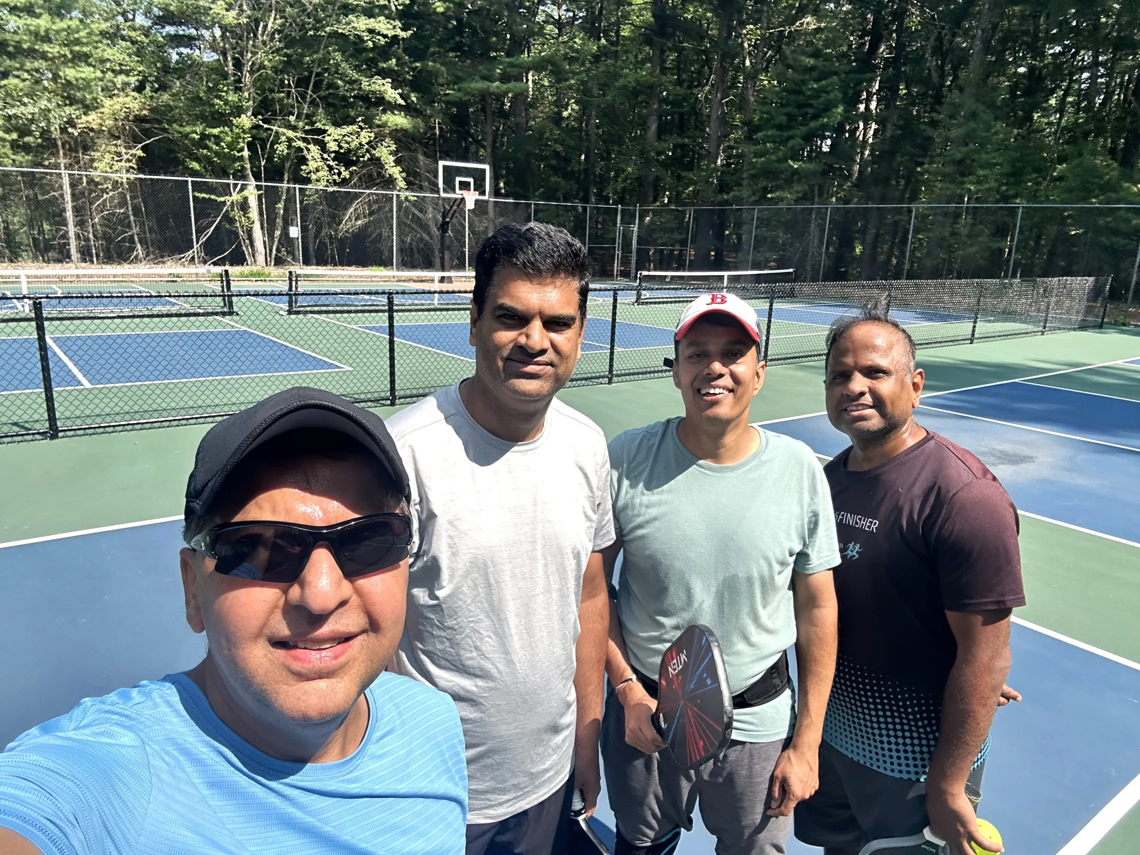 four male friends at an outdoor pickleball court taking a selfie