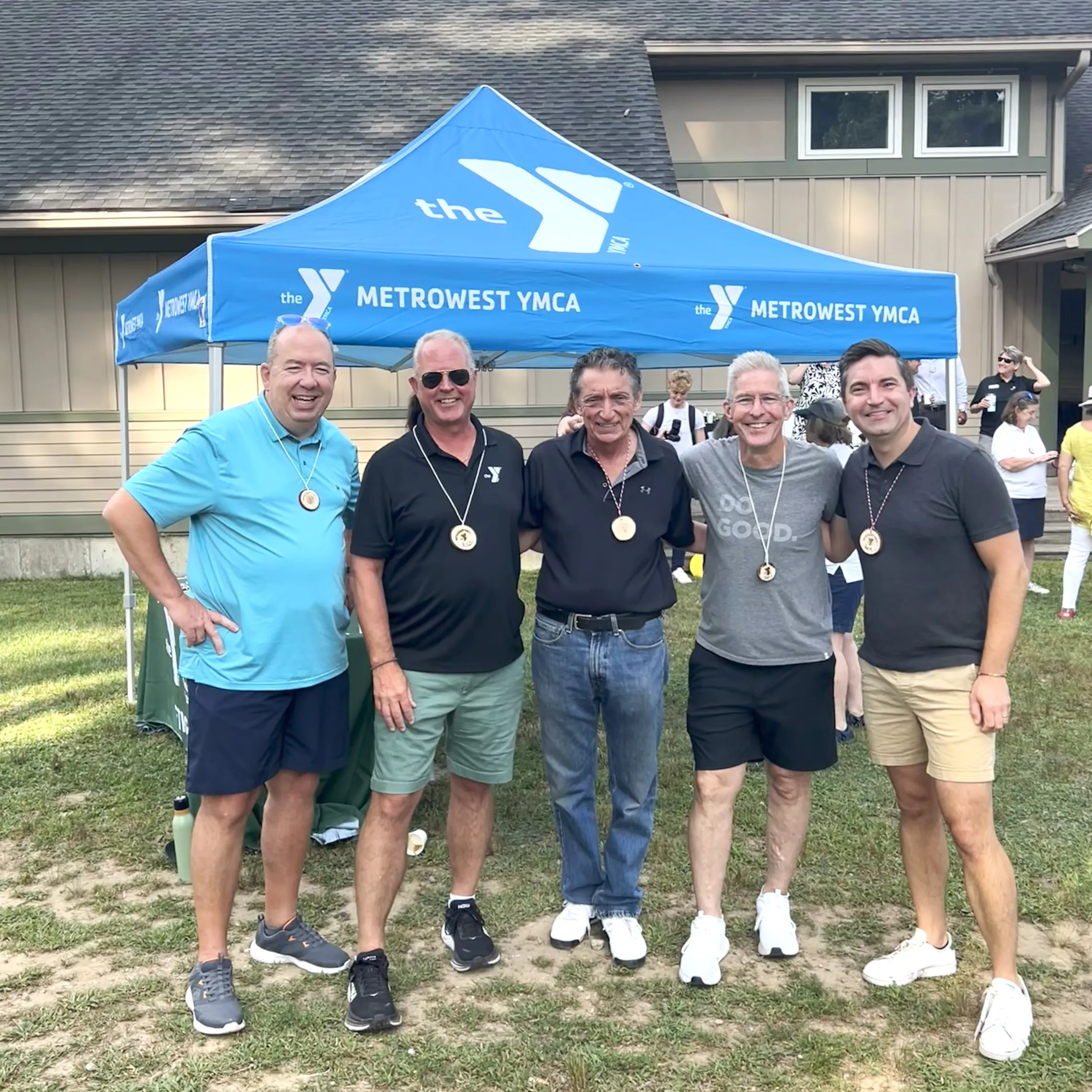 group of five adult males posing for photo, standing in front of blue YMCA tent