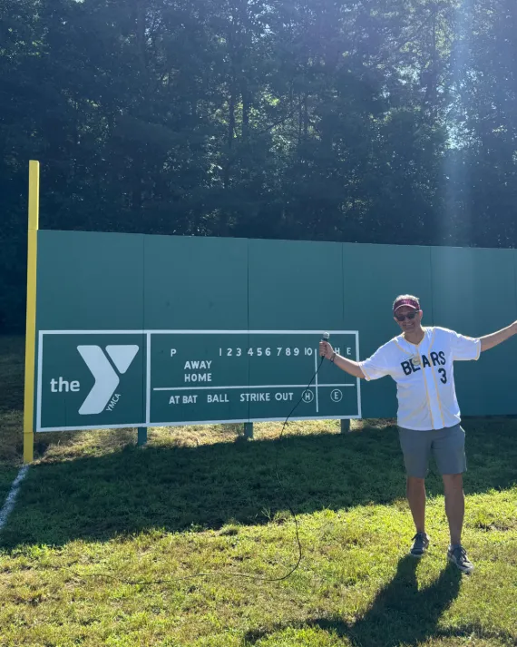 MetroWest YMCA Leader poses in front of the Outdoor Center Green Monster