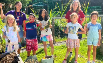 Children in the outdoor center garden harvesting fresh ingredients with their counselors