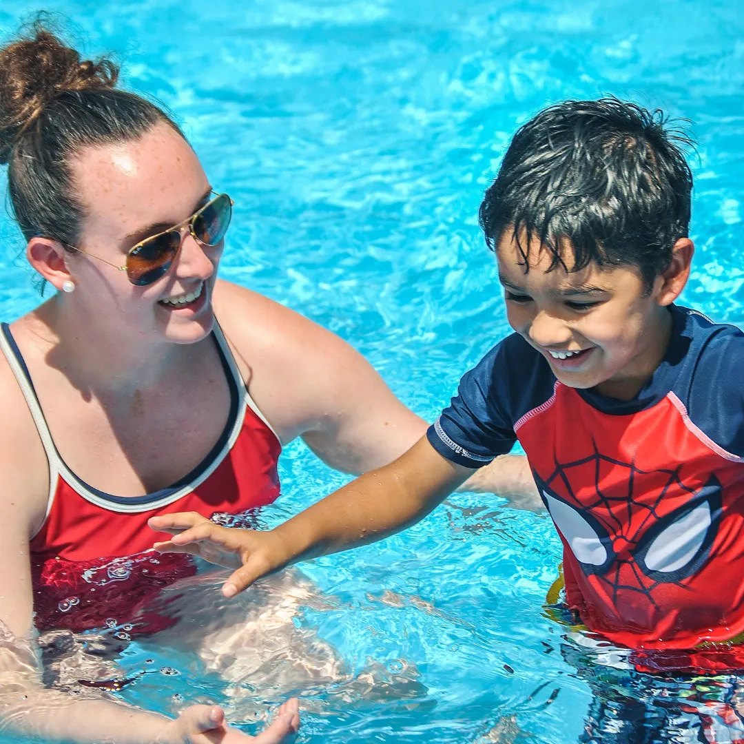 female swim instructor helping young boy in pool